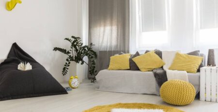 sala decorada em amarelo e cinza com sofás e puffs