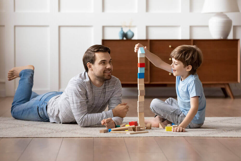 Brincadeiras para tirar as crianças do tédio - Imagem de um pai observando seu bebê brincando e se divertindo dentro de casa
